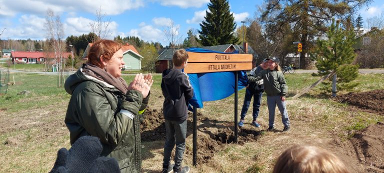 Puuttalan nimikyltin paljastetaan. Kolme koululaista on nostanut sinisen kankaan nimikyltin yläpuolelta ja yleisö taputtaa.