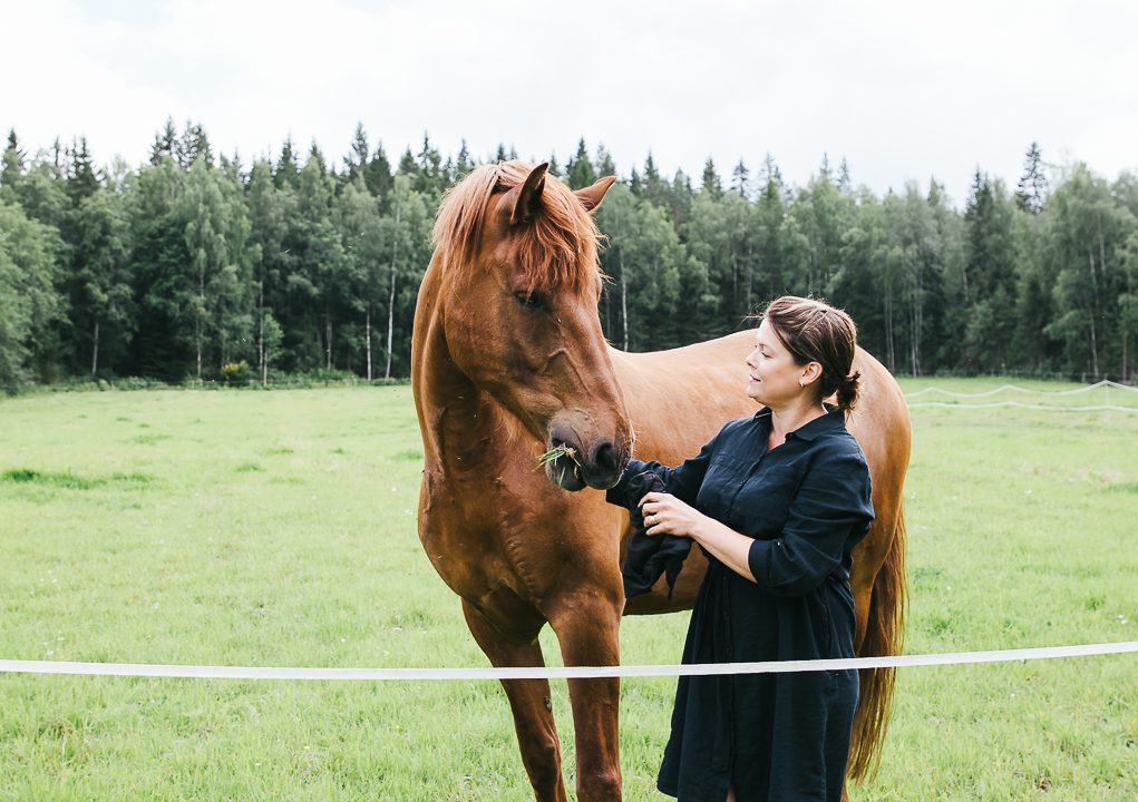 Nainen silittää hevosta laitumella