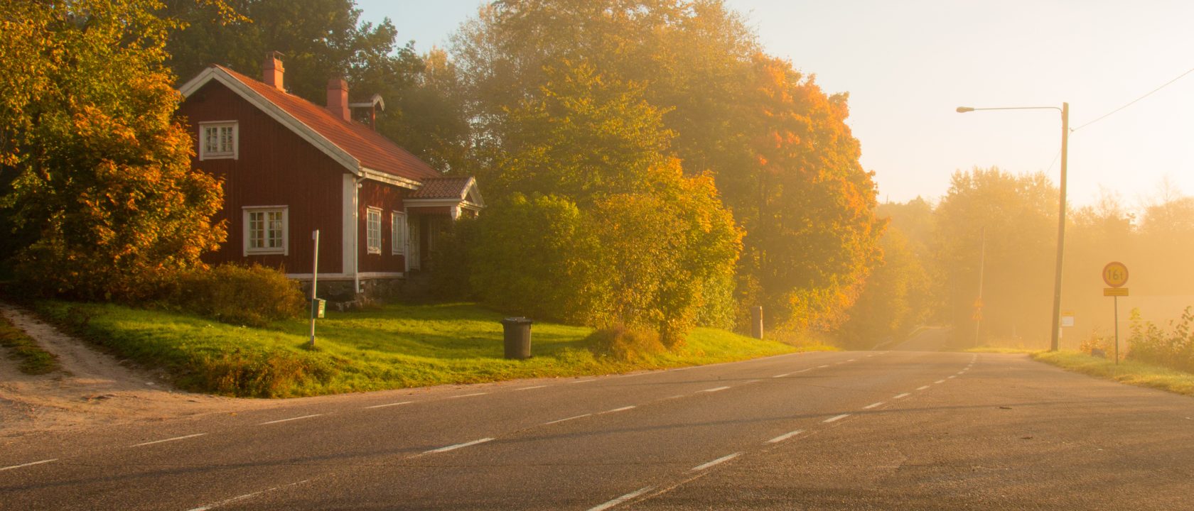 Tien varressa on punainen omakotitalo hieman utuisessa aamussa auringon noustessa.