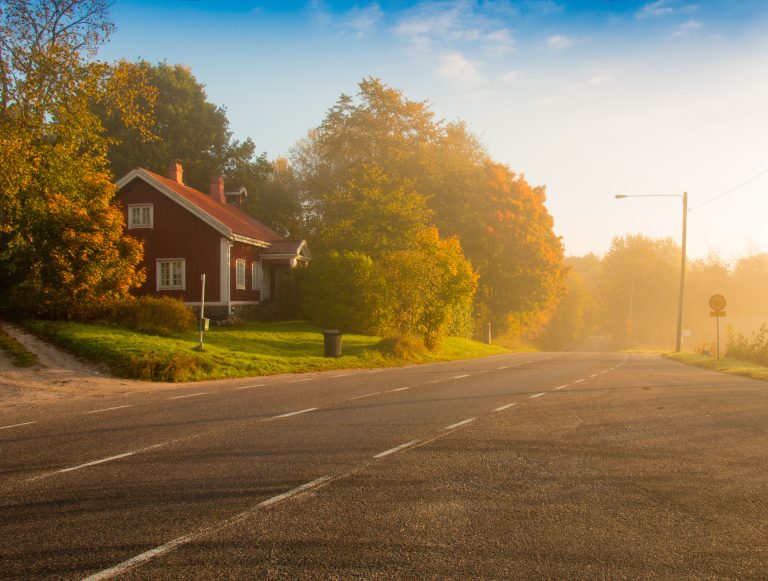 Tien varressa on punainen omakotitalo hieman utuisessa aamussa auringon noustessa.