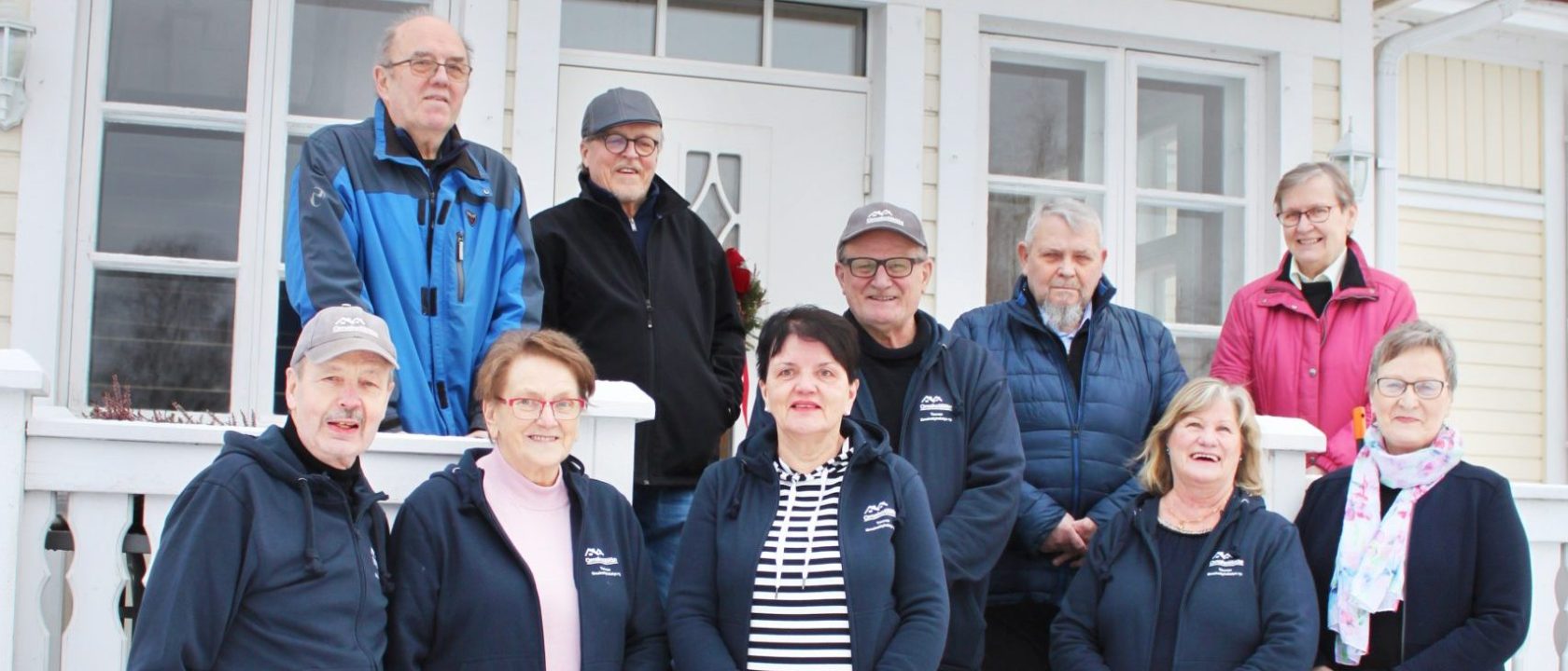 Kuvassa kymmenen henkilöä seisoo talon edustalla. He ovat Pertti Kiuru, Matti Lindfors, Seija Salo, Jarmo Käkelä, Kirsi Siljamäki, Antti Siljamäki, Jorma Salo, Päivi Siljamäki, Eeva Lindfors ja Leila Kiuru.