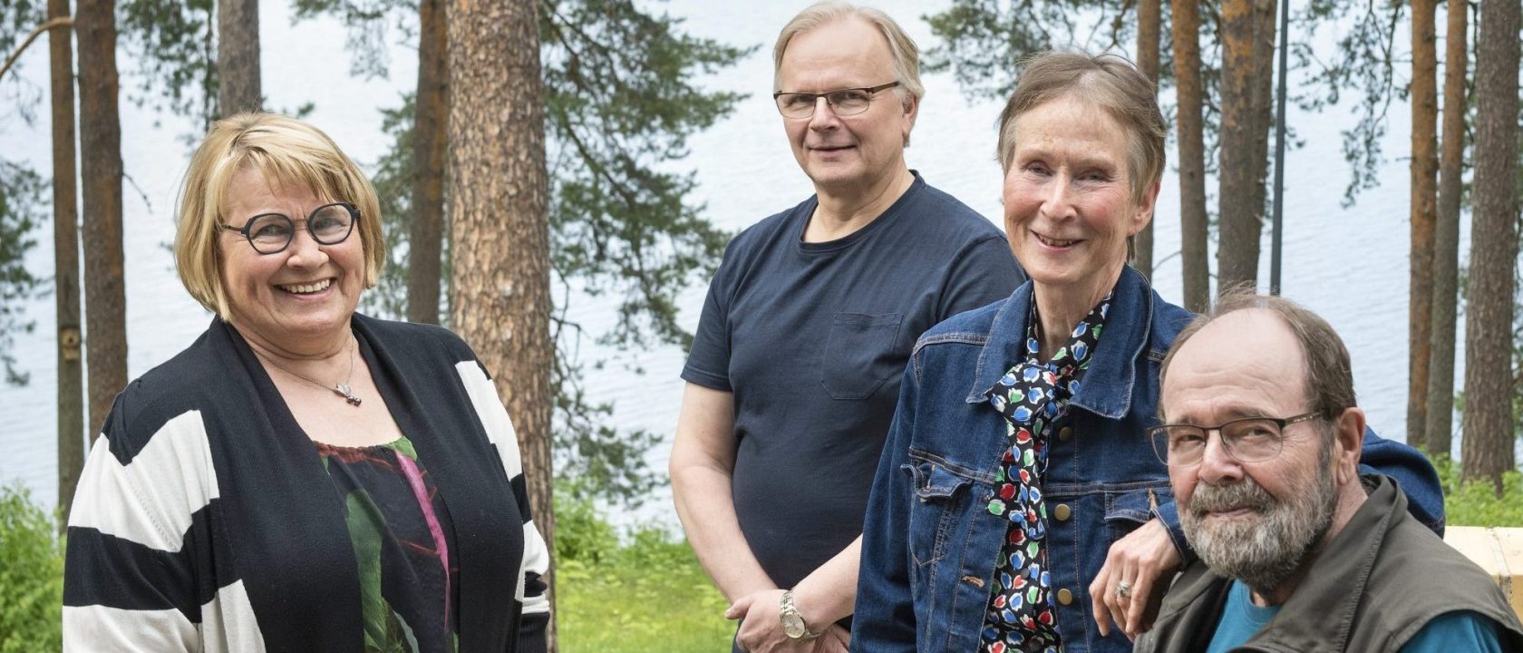 Kuvassa neljä henkilöä seisoo ja taustalla on puita ja järvi.Vasemmalta oikealle puheenjohtaja Anna Hölttä, hallituksen jäsenet Jukka Pihlatie ja Ulla Martin sekä varapuheenjohtaja Matti Pasanen.